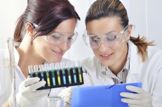 Attractive young PhD students scientists  observing the blue, yellow and green indicator color shift after the solution destillation in chemical laboratory 
