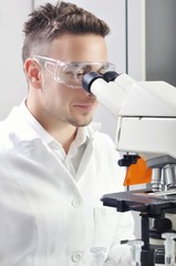 Young scientist studying new substance or virus in microscope