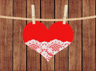 red heart with lace hang on clothespins over wooden planks backg