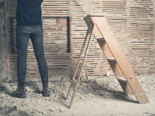 Person standing by wattle and daub walll with ladder