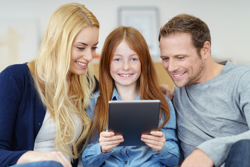 eltern und tochter sitzen auf dem sofa und schauen auf tablet-pc