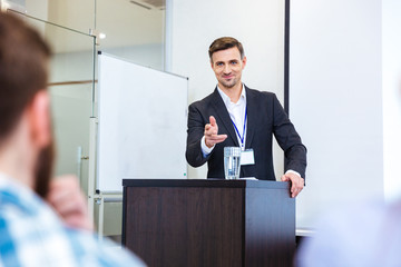 Smiling businessman standing at tribune in conference hall