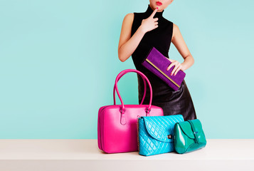 Woman choosing the bag from many colorful bags.Isolated on light blue background. Shopping addiction. 