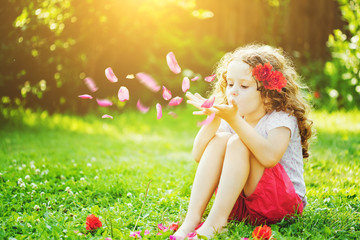 Little girl blowing flower petals from her hands in the sunlight