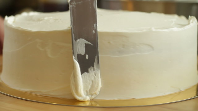 A baker spreads cream on a round cake while he spins it