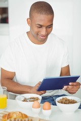 Fototapeta na wymiar Young man using tablet and eating breakfast in kitchen