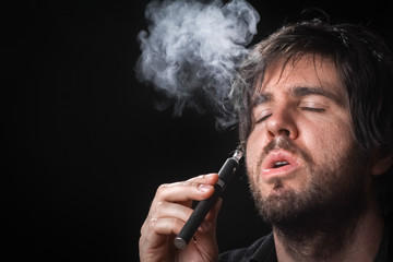 Young man smoking electronic cigarette on black background