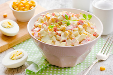 Salad with sticks of surimi, corn, eggs and mayonnaise on white table