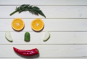 Face made of orange, apple, cucumber, pepper and dill on a kitchen board, on a yellow wooden background. Cheerful face, the concept of healthy eating.