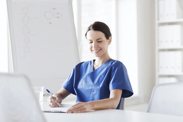 happy female doctor or nurse writing to clipboard