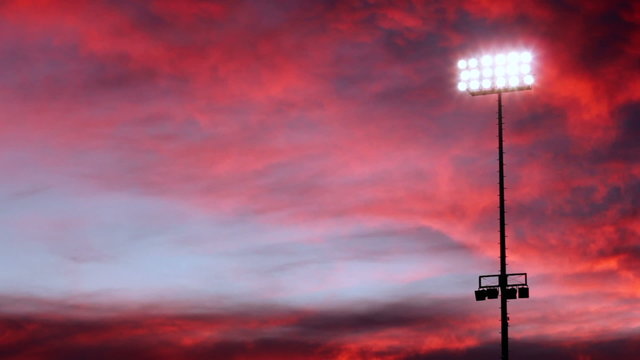 Beautiful pink and purple sky behind one floodlight in a stadium.