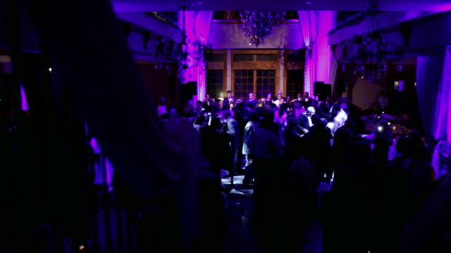 Group of silhouetted people dancing in a dark banquet hall for a wedding reception.