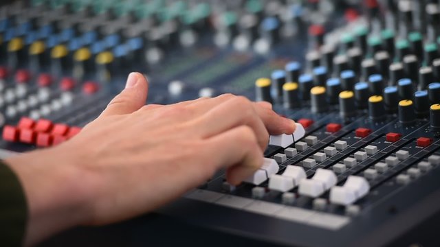 Detail with a hand adjusting sound levels on a professional audio mixer