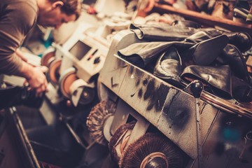 Shoemaker repairs shoes in the studio craft grinder machine.