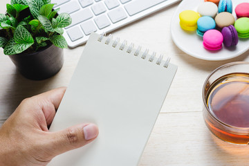 Man holding a book and keyboard with a hot cup of tea, macaroon on the table. Can be attributed to your ad.
