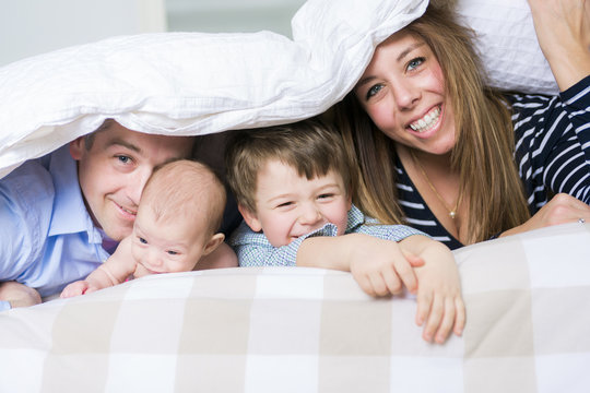 Photo of loving family of four lying on white bed in morning.
