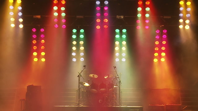 A set of colorful stage lights above a drum kit on an empty stage
