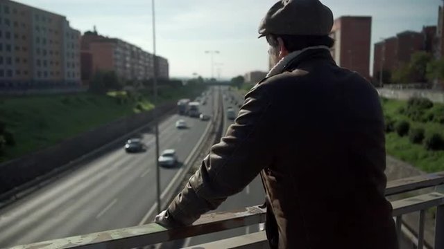 Man looks at traffic in the city in the morning. Dolly shot from a bridge.