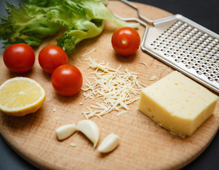 Cheese, tomatoes, garlic with grater on wooden catting board
