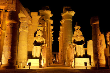 Egypt. Illuminated Luxor Temple. The peristyle courtyard of Ramesses II with two seated granite statues and the processional colonnade of Amenhotep III