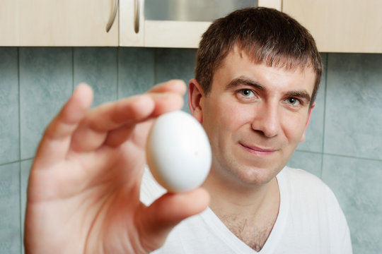Smiling young man holding an egg in his hand, showing it to the camera