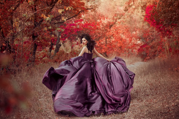 Lady in luxury lush purple dress runs in red wood ,fantastic shot, fairytale girl princess walking in autumn forest, fashionable toning, creative colors. Woman fantasy queen, skirt fabric fly in wind