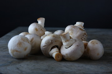 Many small raw unpeeled white champignons with round hats and short stems on brown wooden table