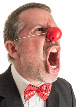 Closeup photograph of a man in a business suit with a red rubber nose and a sparkly red bow tie screaming at the top of his lungs.