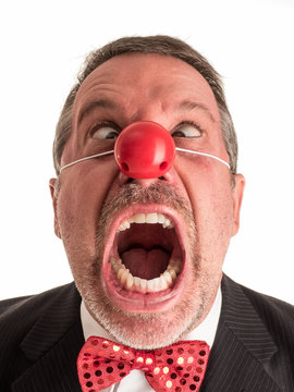 Closeup photograph of a man in a business suit with a red rubber nose and a sparkly red bow tie going coss-eyed while he screams toward the camera.