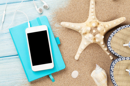 Smartphone and notepad on wood with starfish and shells