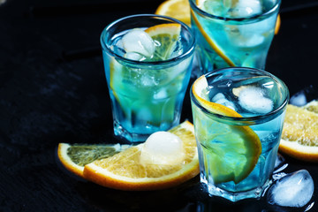 Blue cocktail with ice cubes and slices of orange on a dark back