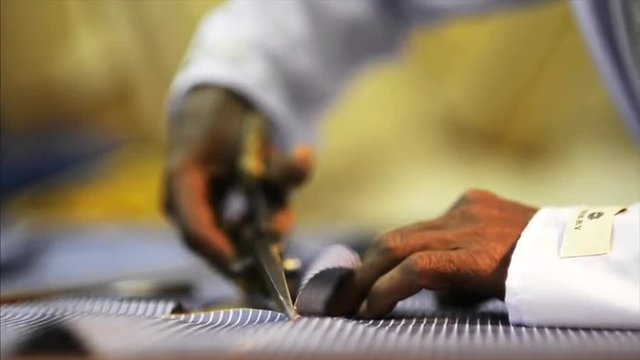 Locked-on shot of a tailor cutting cloth for sewing in textile factory, Kolkata, West Bengal, India