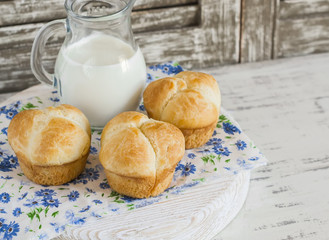 Homemade sweet brioches and milk on rustic light wood background