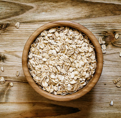Oat flakes in a round bowl on the old wooden background, top vie