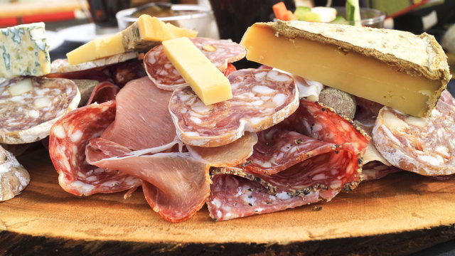 Platter of variety of fresh gourmet cheese, sliced cured meats, sausages, ham