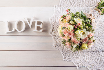 Beautiful wedding bouquet of roses and freesia with letters on white wooden background, background...