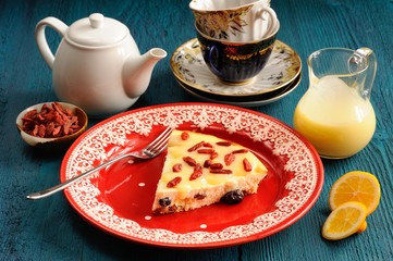 Homemade cheesecake on red plate with lemon curd, tea and goji b