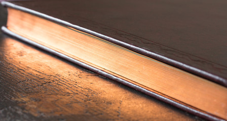 a closed book with gold color edges along the diagonal. shallow depth of field