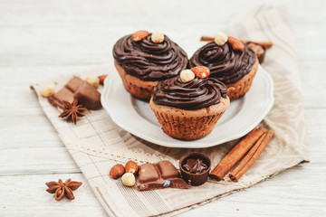 
Chocolate cupcakes with cream , almonds , hazelnuts and cinnamon on a wooden background 