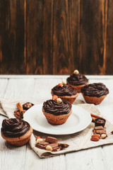 
Chocolate cupcakes with cream , almonds , hazelnuts and cinnamon on a wooden background 