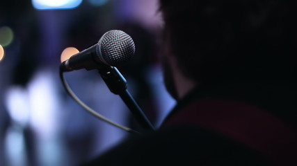 Close-up picture of singer sitting toward a microphone at the stage. Bearded man sitting back to the camera before the show starts. - Powered by Adobe