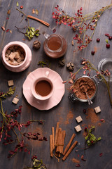 Fototapeta na wymiar Cocoa drink with cinnamon, fresh cocoa powder, cane sugar on rustic wooden background, overhead top view.