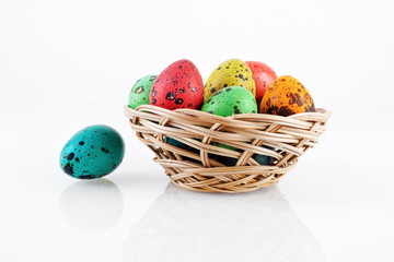 Bright colorful easter eggs. Painted quail eggs in a wicker basket with reflection.