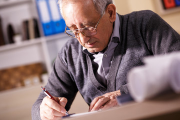 Senior architect working on construction blueprint in office, he draws with a pencil and ruler.