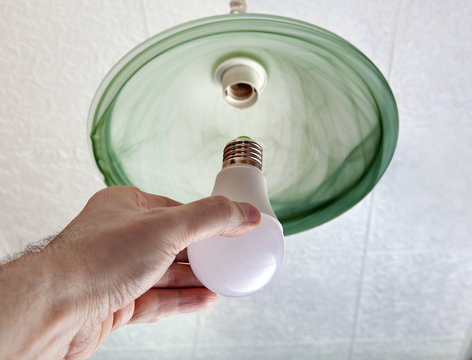 Installing LED light bulb in ceiling light, hand holding lamp.