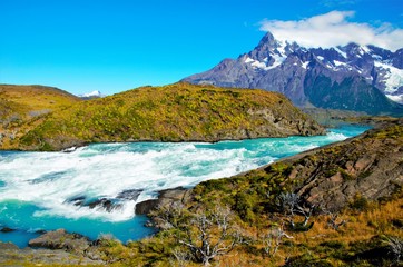 SALTO GRANDE, TORRES DEL PAINE NATIONAL PARK, CHILE - FEBRUARY, 5, 2016: Waterfall between green and brown hills, in the background snow covered mountain