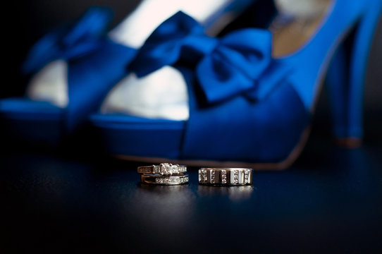 wedding rings in front with blue wedding shoes 