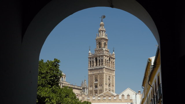 La Giralda Tower, in Seville, Andalusia, Spain, seen through an arch with a blue sky. The shot starts from a deep shadow.