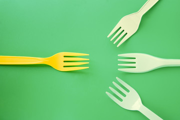 White plastic forks appearing to come together to battle yellow fork on a green background