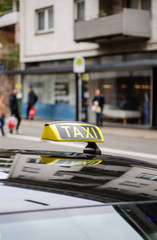 Obraz premium Taxi sign waiting for customers in city with defocused pedestrians and city background 